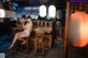 A woman sitting on a stool in front of a bar.