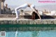 A woman doing a yoga pose by a swimming pool.