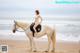 A woman in a bikini riding a horse on the beach.