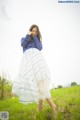 A woman in a blue shirt and white skirt standing in a field.