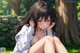 Anime girl sitting on the grass in a park.