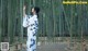 A woman in a blue and white kimono standing in a bamboo forest.